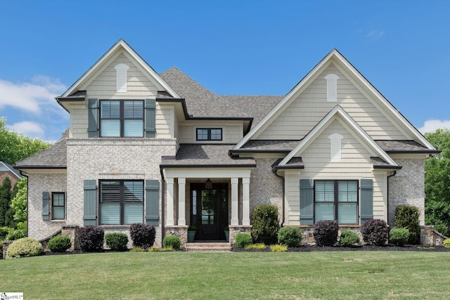 craftsman inspired home with a shingled roof, a front lawn, and stone siding