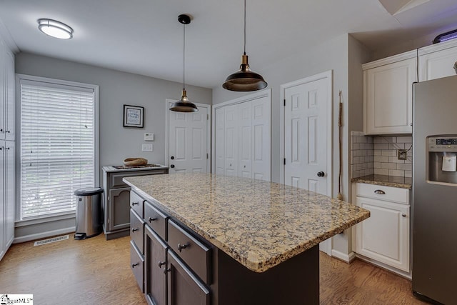 kitchen featuring light stone countertops, stainless steel fridge, decorative backsplash, light wood-type flooring, and visible vents