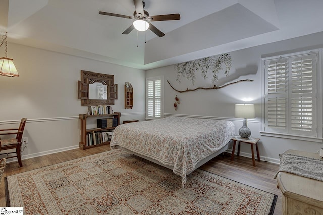 bedroom with baseboards, a tray ceiling, ceiling fan, and wood finished floors