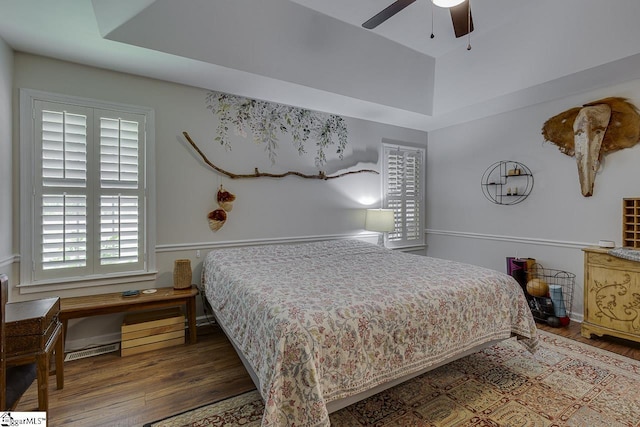 bedroom with a raised ceiling, ceiling fan, and wood finished floors
