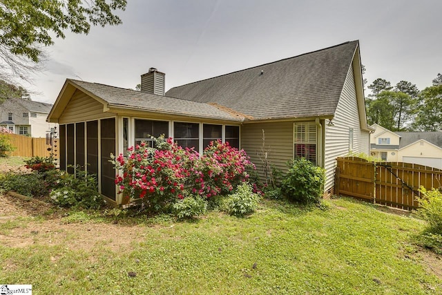rear view of property featuring fence, a chimney, a sunroom, a shingled roof, and a yard