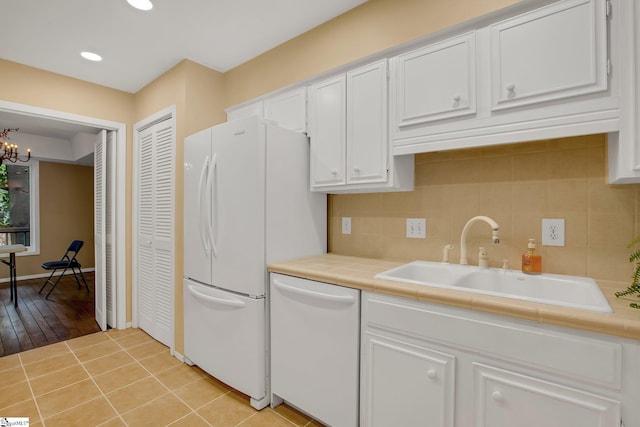 kitchen with decorative backsplash, white appliances, white cabinetry, a chandelier, and a sink