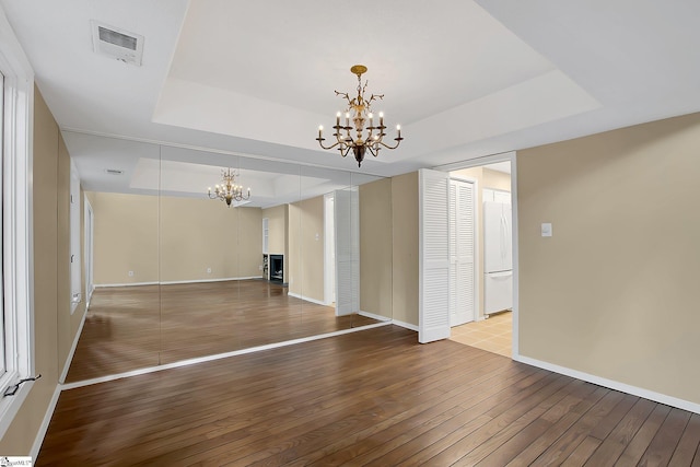 unfurnished living room featuring an inviting chandelier, a raised ceiling, hardwood / wood-style floors, baseboards, and visible vents