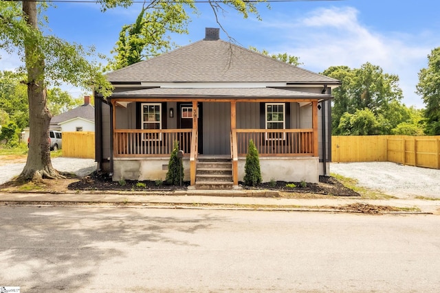bungalow-style house with fence, a shingled roof, a chimney, and a porch