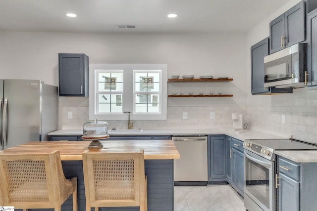 kitchen with visible vents, marble finish floor, a kitchen island, butcher block countertops, and appliances with stainless steel finishes