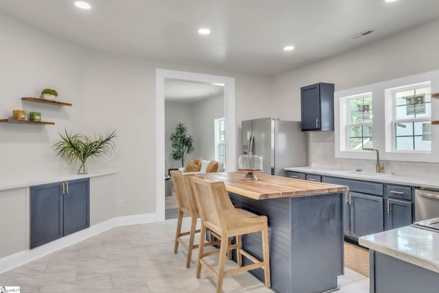 kitchen featuring appliances with stainless steel finishes, a sink, recessed lighting, a kitchen bar, and visible vents
