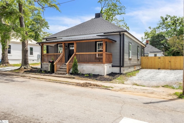 bungalow-style home featuring covered porch, fence, a shingled roof, and a chimney