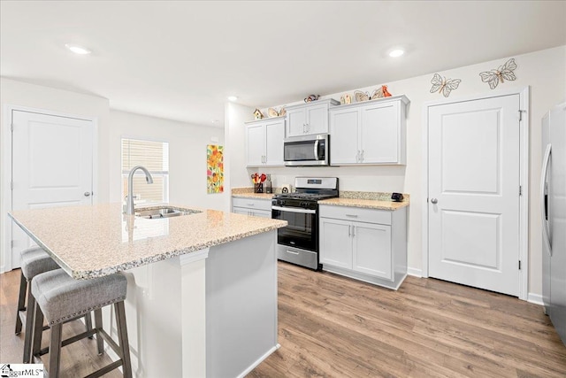kitchen with a sink, a breakfast bar area, an island with sink, light wood-style flooring, and stainless steel appliances