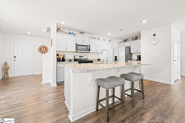 kitchen with an island with sink, a kitchen breakfast bar, a sink, light wood finished floors, and appliances with stainless steel finishes