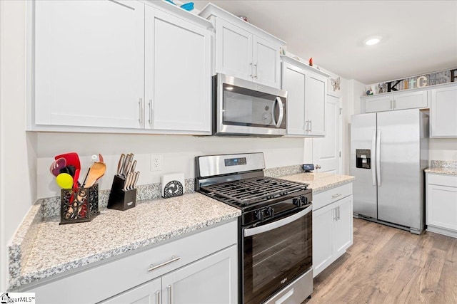 kitchen featuring white cabinets, stainless steel appliances, light stone counters, and light wood-type flooring