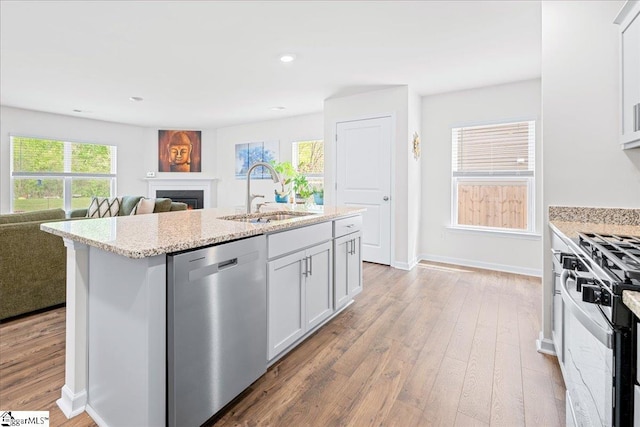 kitchen with a fireplace, white cabinets, a sink, light wood finished floors, and appliances with stainless steel finishes