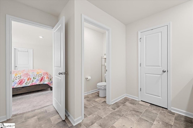 bathroom with baseboards, stone finish floor, toilet, and ensuite bath