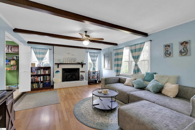 living area featuring a ceiling fan, a brick fireplace, beam ceiling, wood finished floors, and ornamental molding
