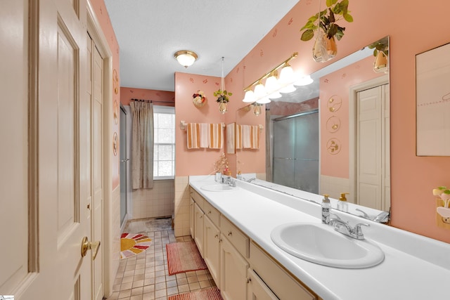 bathroom with double vanity, a shower stall, a sink, and tile patterned flooring