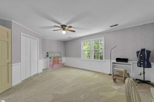playroom with carpet flooring, a wainscoted wall, a ceiling fan, visible vents, and ornamental molding