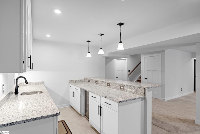 kitchen with a sink, baseboards, light stone counters, a peninsula, and white cabinetry