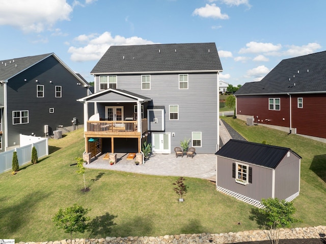rear view of house featuring a deck, a patio, french doors, a lawn, and an outbuilding