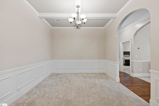empty room featuring arched walkways, a chandelier, a wainscoted wall, visible vents, and ornamental molding