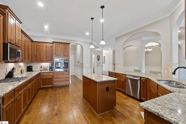 kitchen with light stone countertops, a center island, arched walkways, a sink, and appliances with stainless steel finishes