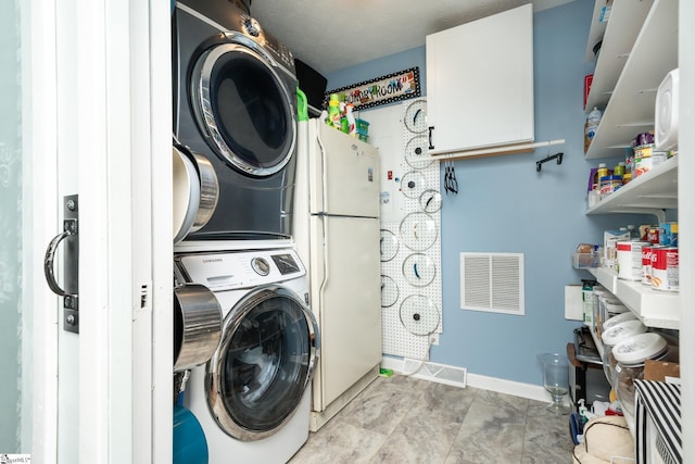clothes washing area with stacked washer / drying machine, visible vents, and baseboards