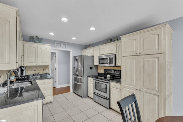 kitchen with a sink, appliances with stainless steel finishes, light tile patterned floors, and backsplash