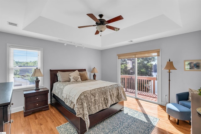bedroom with visible vents, track lighting, a raised ceiling, light wood-style floors, and access to outside