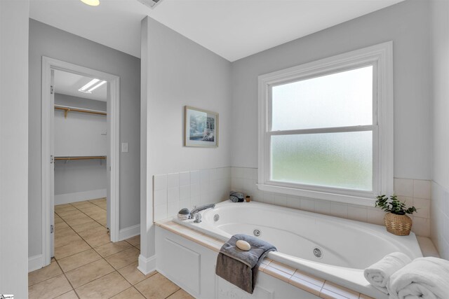 bathroom featuring tile patterned flooring, baseboards, a spacious closet, and a tub with jets