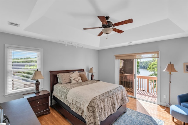 bedroom featuring access to exterior, visible vents, rail lighting, light wood-style floors, and a tray ceiling