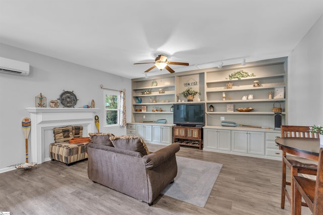 living area with ceiling fan, track lighting, light wood finished floors, a glass covered fireplace, and a wall unit AC