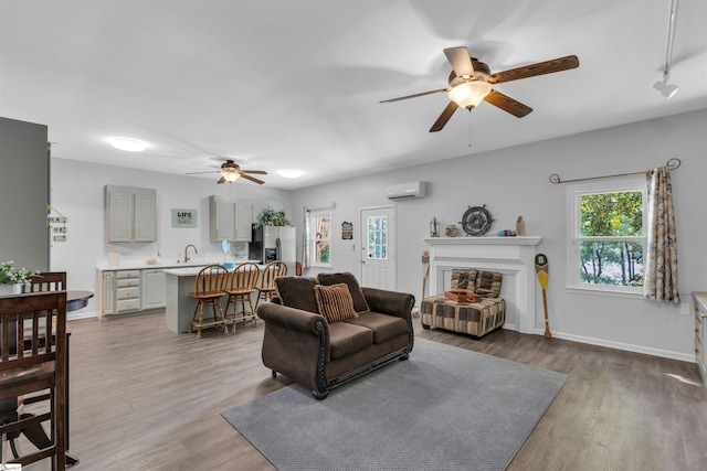 living room featuring baseboards, ceiling fan, a wall unit AC, and wood finished floors