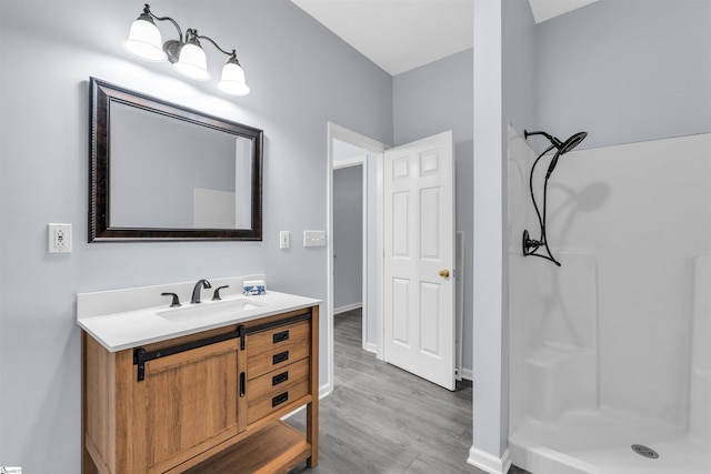 bathroom with a walk in shower, vanity, baseboards, and wood finished floors