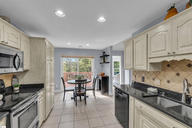 kitchen with a sink, baseboards, light tile patterned floors, stainless steel appliances, and cream cabinetry