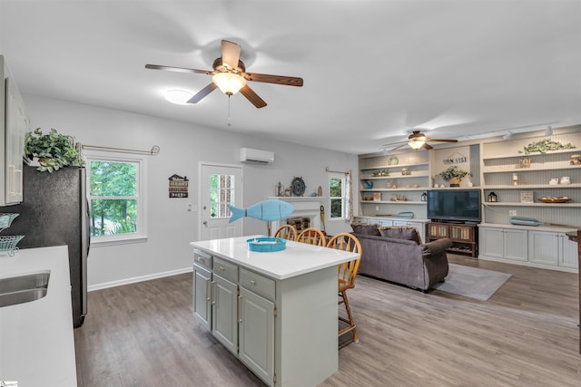 kitchen featuring a ceiling fan, a center island, light wood-type flooring, an AC wall unit, and a breakfast bar