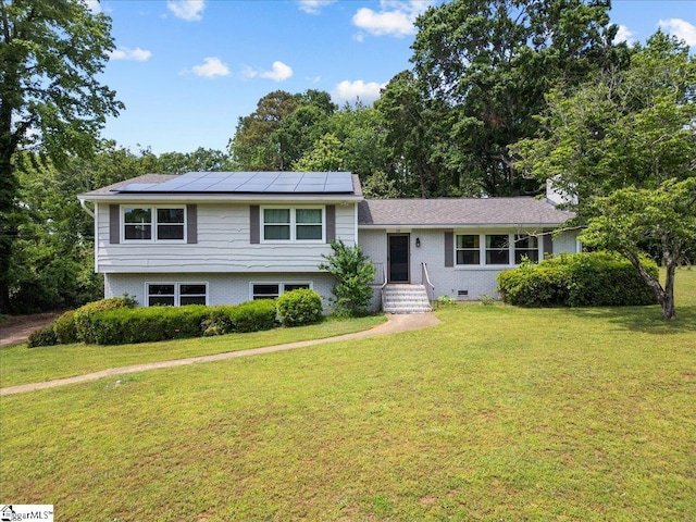 split level home featuring roof mounted solar panels, a front lawn, and brick siding
