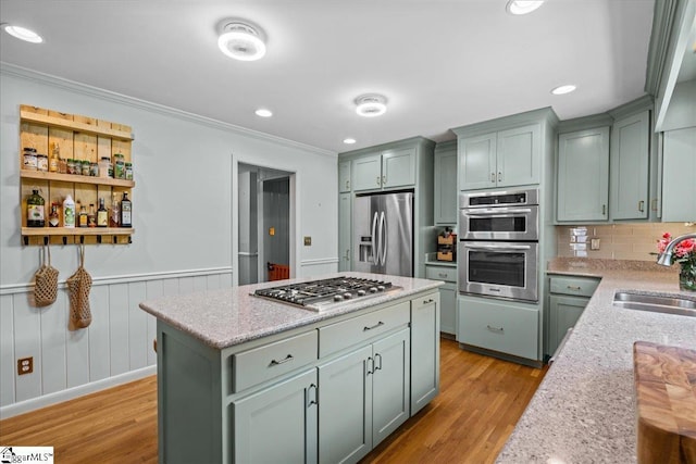 kitchen with appliances with stainless steel finishes, light wood-type flooring, a sink, green cabinets, and ornamental molding