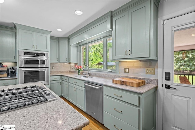 kitchen featuring stainless steel appliances, green cabinetry, decorative backsplash, and a sink