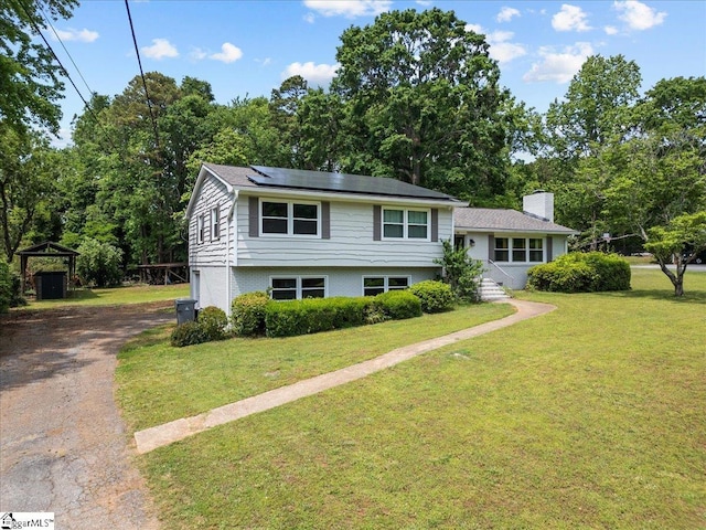 split level home with roof mounted solar panels, a front lawn, aphalt driveway, and a chimney