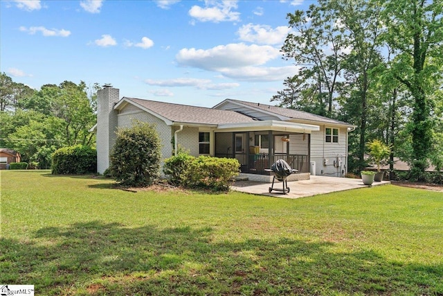 rear view of house featuring a chimney, a sunroom, a patio area, brick siding, and a yard