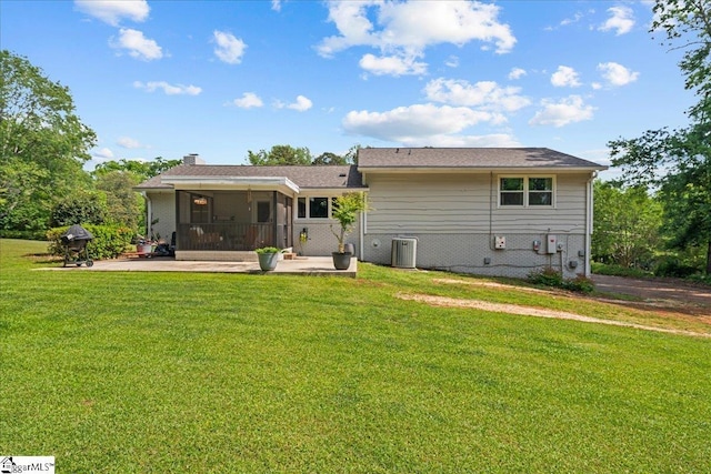 back of house featuring a sunroom, a chimney, cooling unit, a patio area, and a lawn