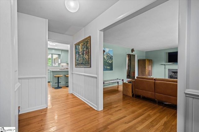 hallway featuring light wood finished floors, a decorative wall, and wainscoting
