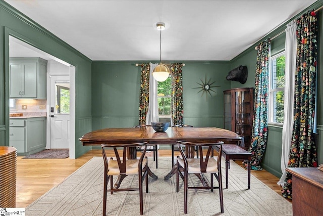 dining room with light wood-type flooring, crown molding, and a wainscoted wall