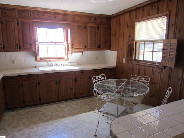 kitchen with a sink, wood walls, brown cabinetry, light floors, and backsplash