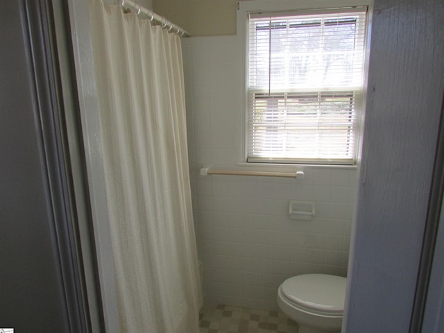 bathroom with curtained shower, toilet, and tile walls