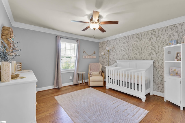 bedroom featuring a nursery area, baseboards, light wood-style floors, ornamental molding, and wallpapered walls