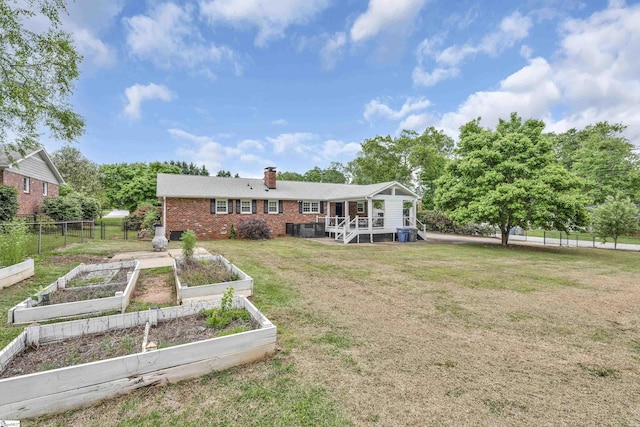 back of property with fence, brick siding, a vegetable garden, a chimney, and a lawn