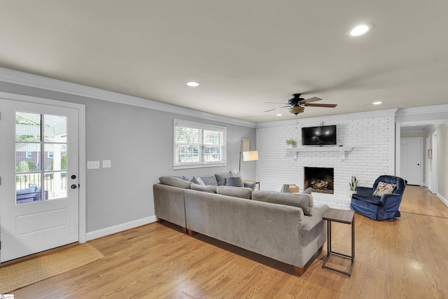 living room featuring crown molding, a ceiling fan, a brick fireplace, and light wood-style flooring