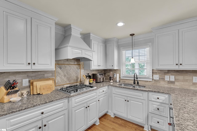 kitchen with premium range hood, white cabinets, tasteful backsplash, a sink, and stainless steel gas stovetop