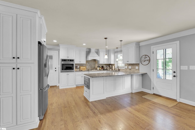 kitchen featuring white cabinets, appliances with stainless steel finishes, a peninsula, custom range hood, and tasteful backsplash