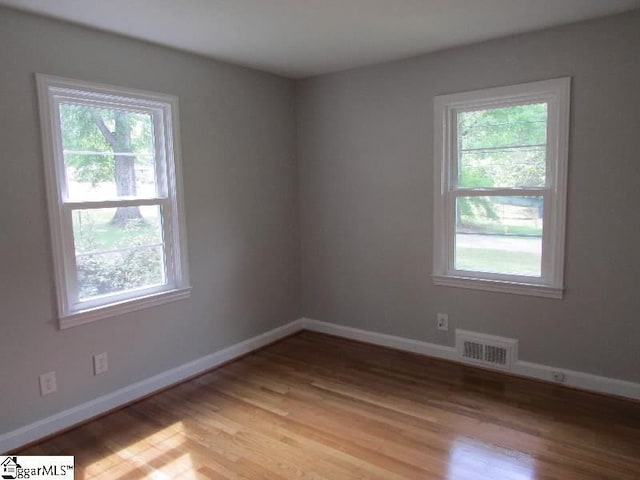 empty room with visible vents, a wealth of natural light, and light wood finished floors