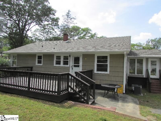 rear view of property with a chimney, roof with shingles, a deck, a patio area, and central AC